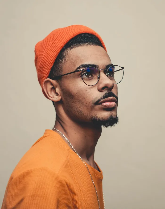 Portrait of a young man in an orange beanie, glasses and an orange top.